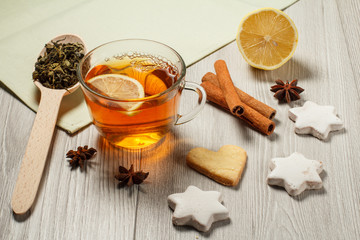 Cup of tea with slice of lemon, gingerbread cookies in star and heart shape, wooden spoon with leaves of green tea and spices