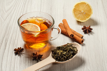 Cup of tea with slice of lemon, wooden spoon with leaves of green tea and spices