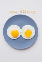 two eggs on a plate and a yellow napkin, inscription Good Morning