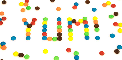 Yum word written with colorful button shaped chocolates candy isolated