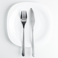 cutlery, fork and knife on an empty white plate on a white backg