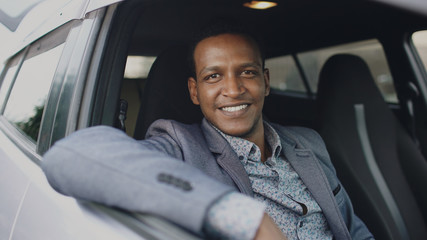 Portrait of serious businessman sitting inside car and smiling into camera outdoors