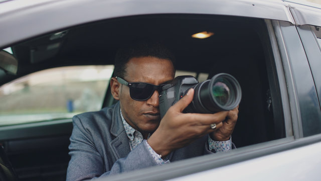 Paparazzi man sitting inside car and photographing with dslr camera
