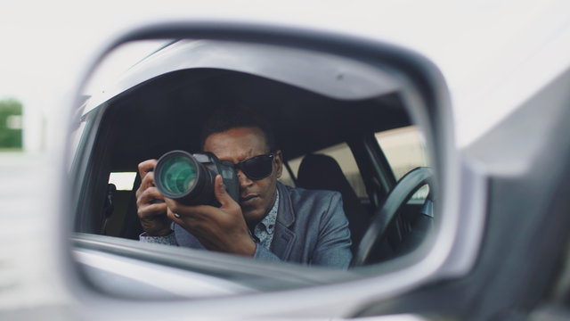 Reflection in side mirror of Paparazzi man sitting inside car and photographing with dslr camera