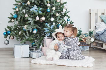 Two little sister girls open their gifts at the Christmas tree in the morning on the deck