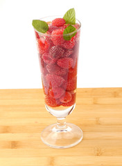 Glass of water full with raspberries isolated on wooden plank