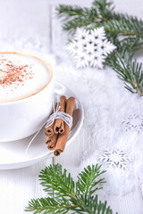 Winter coffee cappuccino and christmas tree branches. White cup of cappuccino with cinnamon on a wooden background