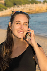 Beautiful woman with blue eyes talking on mobile cell phone on the beach at sunset