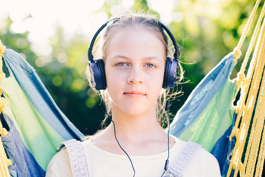 Cute girl listening to music with headphones outdoor - looking at camera