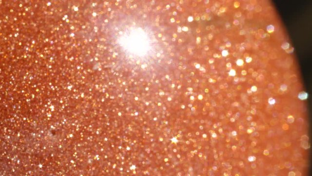 MACRO DOF: Beautiful orange sunstone sphere with golden specks sparkling in sunlight. Sunstone semi precious stone glittering in sunlight. Reflective golden round stone emitting strong rays of light.