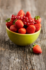 Erdbeeren und Johanisbeeren in einer grünen Schale auf einem rustikalen Holzuntergrund