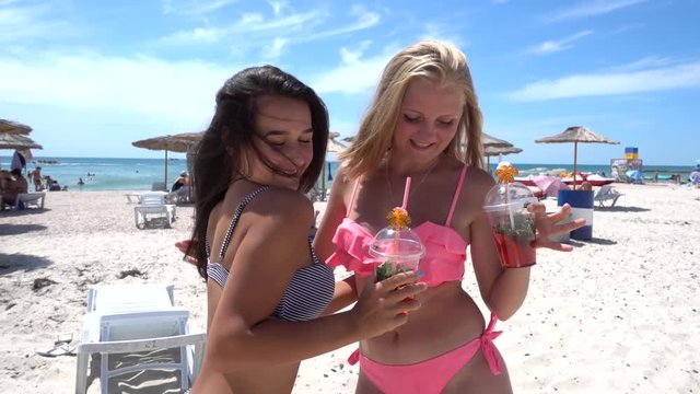 Two girls Drink Cocktails Have Fun Crazy Laughing on the Sea Summer Beach