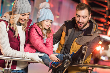 happy parents looking at cute little daughter wearing skates on rink