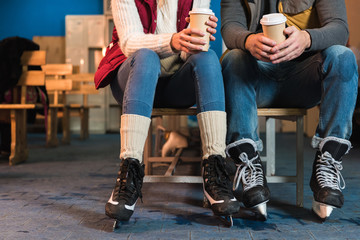cropped shot of young couple in skates holding coffee to go in paper cups
