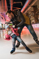 father teaching cute little daughter skating on rink