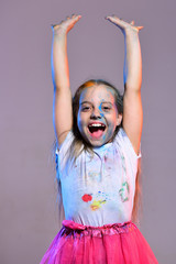 Kid with ponytails holds hands up. Schoolgirl has paint spots