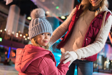 Fototapeta premium cropped shot of smiling mother and adorable little daughter holding hands on rink