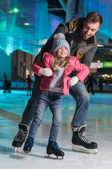 Obraz na płótnie Canvas happy father hugging adorable little daughter on skating rink
