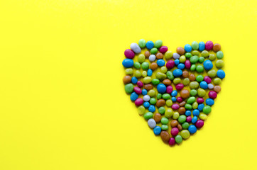 heart from multicolored candy on yellow background