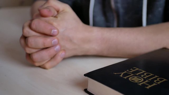 The person prays with his fingers crossed near the Holy Bible lying on the table