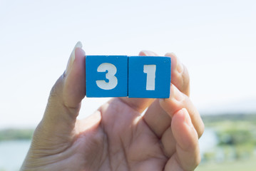 Women's hand Holding Thirty-one number on blue sky background.