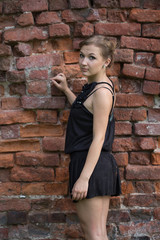 Young blond woman wearing black dress standing over brick wall. Half-length.