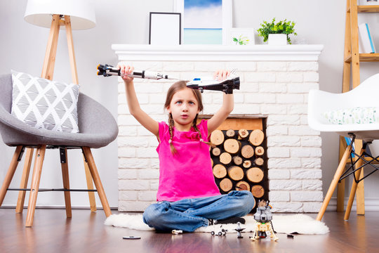 Young child girl female playing with cosmos's toys constructor: rocket, shuttle, rover, satellite and astronaut doll in comfortable interior at home on wooden floor