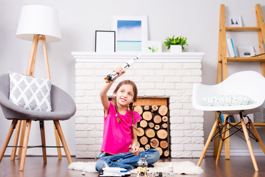 Young child girl female playing with cosmos's toys constructor: rocket, shuttle, rover, satellite and astronaut doll in comfortable interior at home on wooden floor