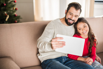 father and daughter taking selfie sitting on sofa at home