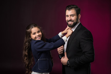 smiling daughter fixing father tie and looking at camera on burgundy