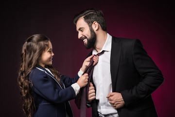 smiling daughter fixing father tie on burgundy