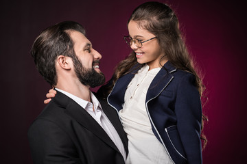 smiling father and daughter looking at each other on burgundy