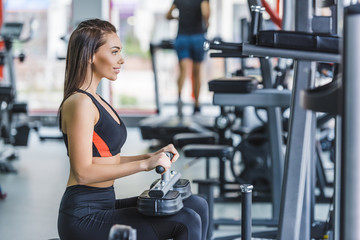 Fototapeta premium young athletic woman sitting on gym machine and looking away