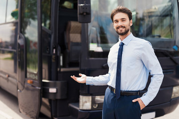 A male driver smiling and posing against a black tourist bus. Behind the back is a modern black tourist bus.