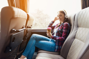 The woman on the passenger seat of the bus listens to music and drinks coffee. © Vadym Huzhva