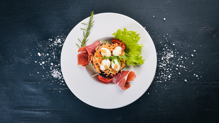 Salad with prosciutto, quail eggs, prunes and fresh vegetables on the plate. On a wooden background. Top view. Free space for text.