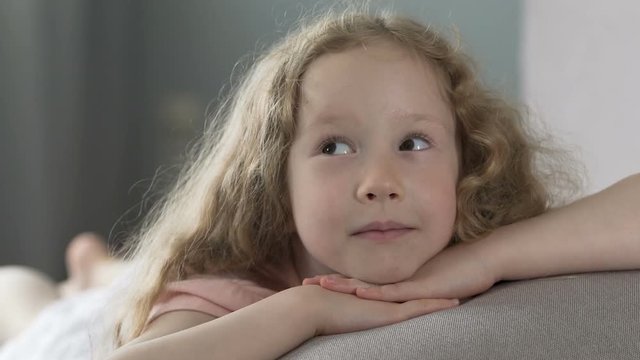 Happy child lying on couch and smiling, looking at her parents with love