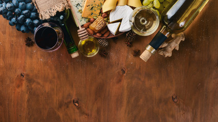A bottle of wine, and a large assortment of cheeses, honey, nuts and spices, on a wooden table. Top view. Free space for text.
