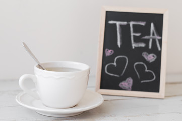 Romantic tea break: hot beverage in white small cup served with framed chalkboard with handwritten hearts and text 