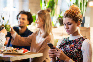woman with smartphone and friends at restaurant