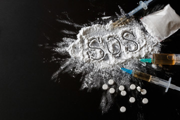 Narcotics heroin, syringes, money on a dark background with the inscription sos and copy space, the concept of crime and drug addiction
