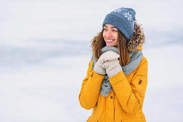 Close up portrait of beautiful smiling girl in yellow winter jacket on the snowy background.