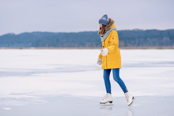 Fototapeta na wymiar Young beautiful girl in yellow jacket is skating at winter on a frozen lake.
