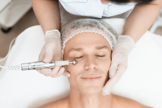 A man came to laser hair removal facial. Doctor leads him in the face with a modern laser epilator.