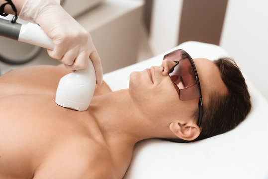 The man came to the procedure of laser hair removal. The doctor treats his neck and face with a special apparatus.