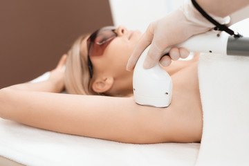 The woman came to the procedure of laser hair removal. The doctor treats her armpits with an...