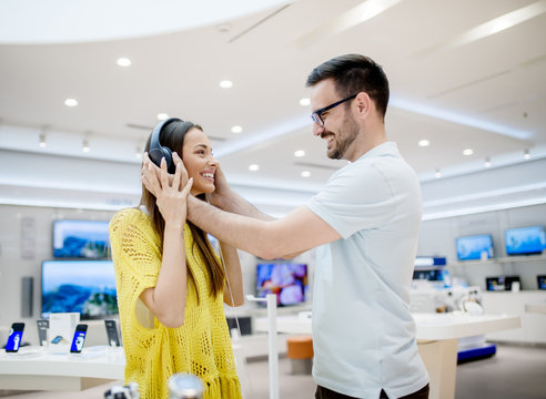 Side view of beautiful young stylish adorable love couple testing headphones in a tech store.