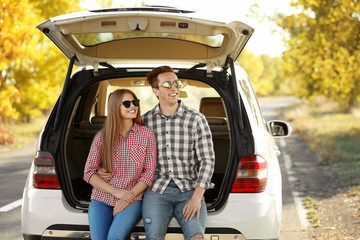Beautiful young couple sitting in car trunk