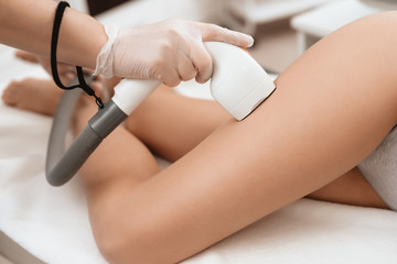 The woman came to the procedure of laser hair removal. The doctor treats her thigh with a device.