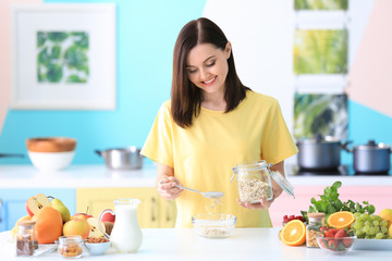 Obraz na płótnie Canvas Young woman preparing oatmeal porridge on table in kitchen